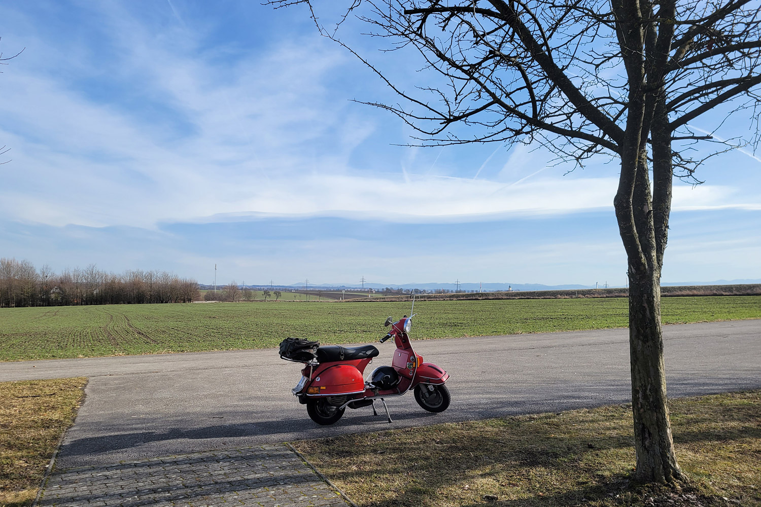 Rote Vespa vor kahlen Feldern im Frühjahr